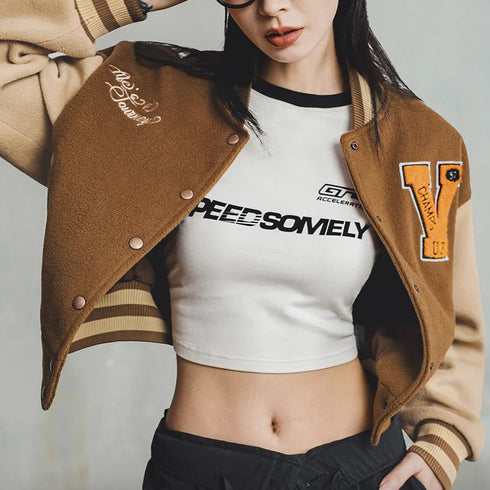 Person wearing a brown letterman jacket over a white crop top with text, on a plain background